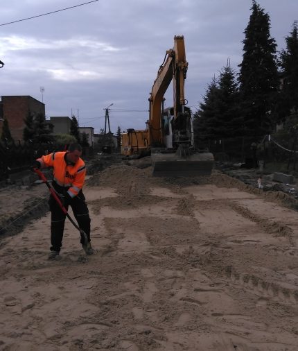 Pracownik budowlany oraz koparka rozprowadzający piasek pod nawierzchnię jezdni